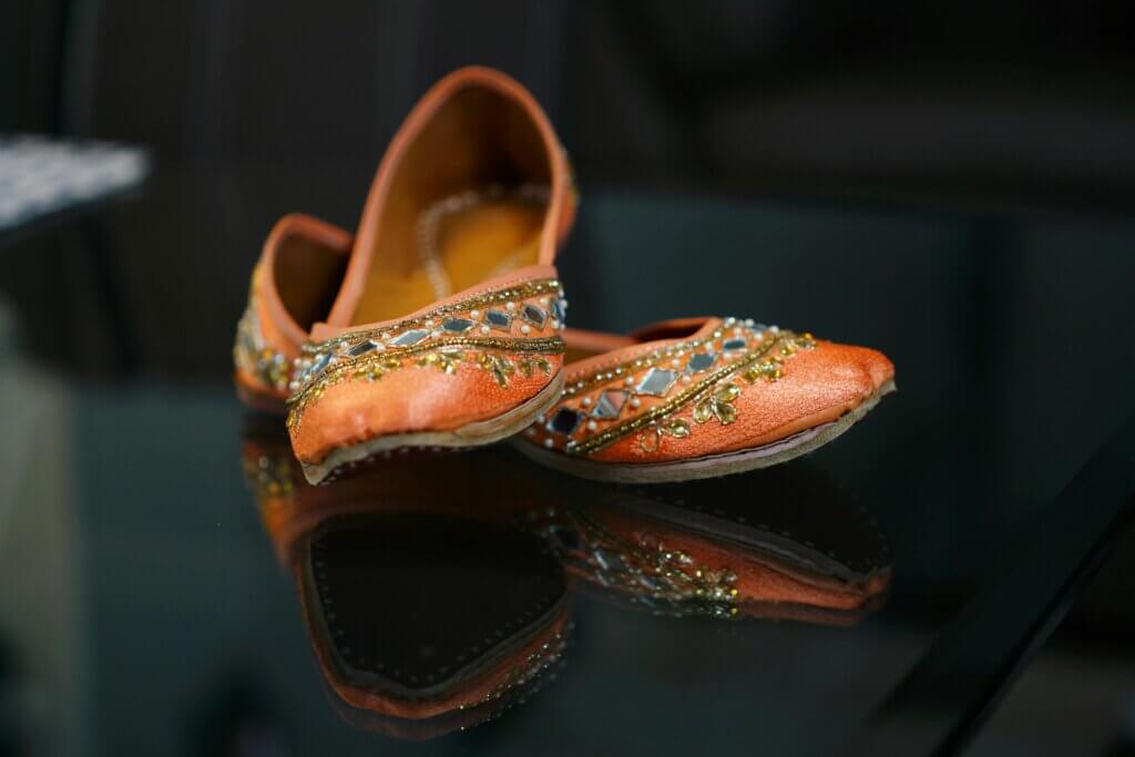 pexels-photo-6387629-6387629 Intricately embroidered traditional jutti shoes placed elegantly on a reflective glass surface.