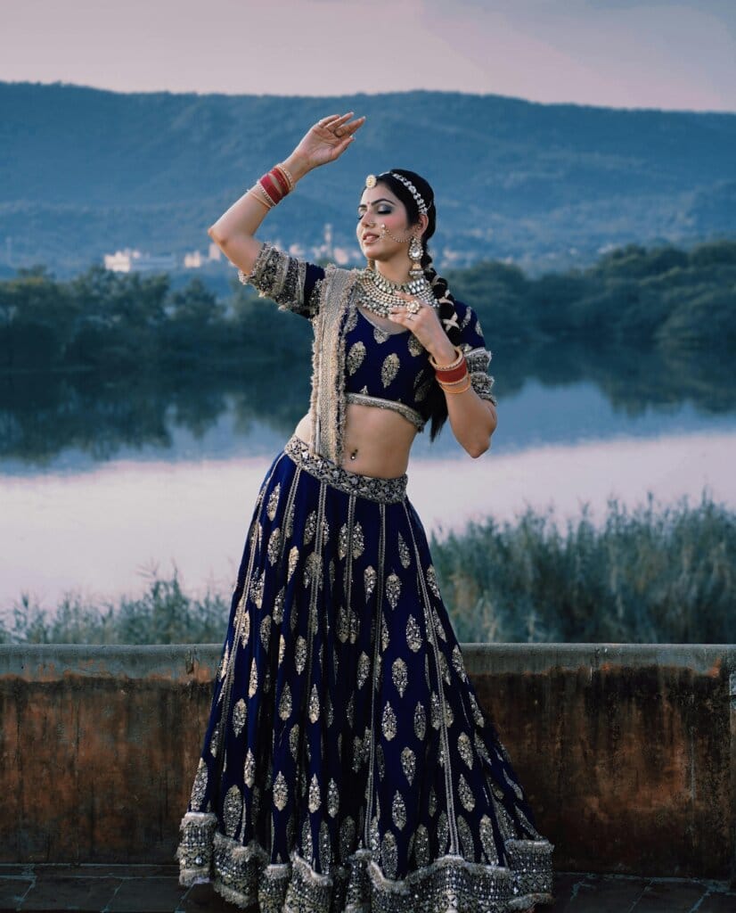 pexels-photo-28867971-28867971 A woman in traditional Indian attire poses gracefully by a serene lakeside with mountains in the background.