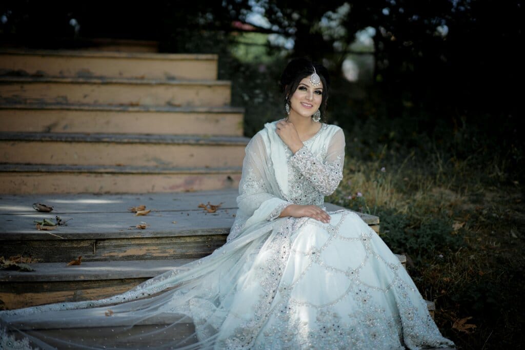 pexels-photo-8531991-8531991 A beautiful Indian bride wearing an elegant bridal gown, sitting outdoors on wooden steps.