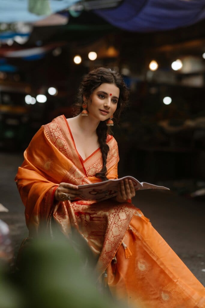pexels-photo-28943484-28943484 Beautiful woman in an orange saree reading a magazine at night market.