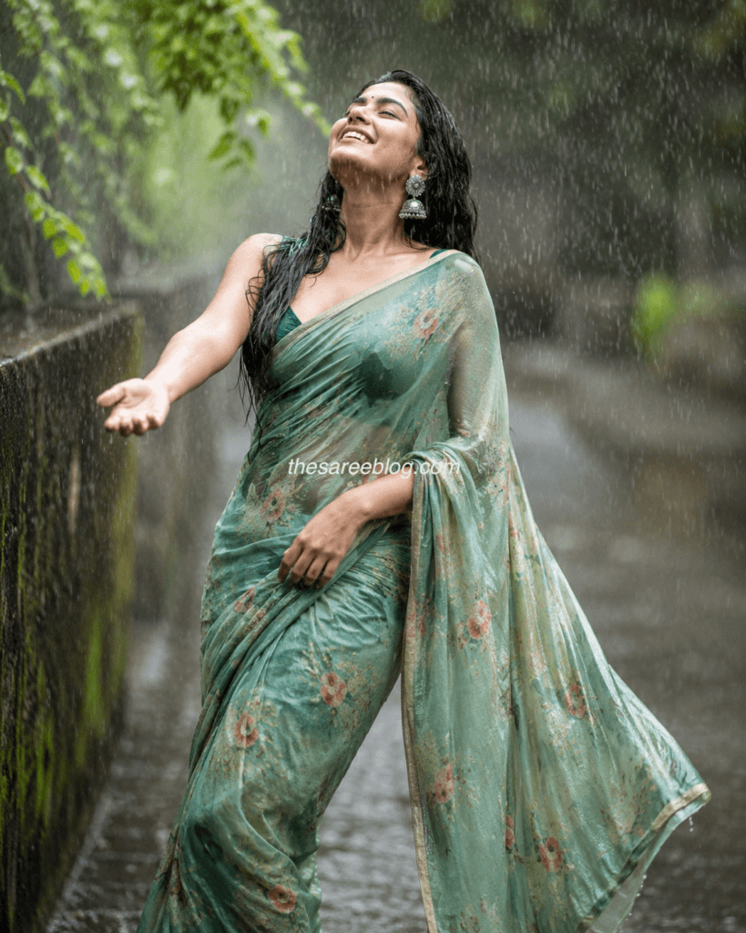 Woman wearing a teal georgette saree with a printed blouse, walking confidently on a rain-soaked street during the monsoon with a chic crossbody bag.