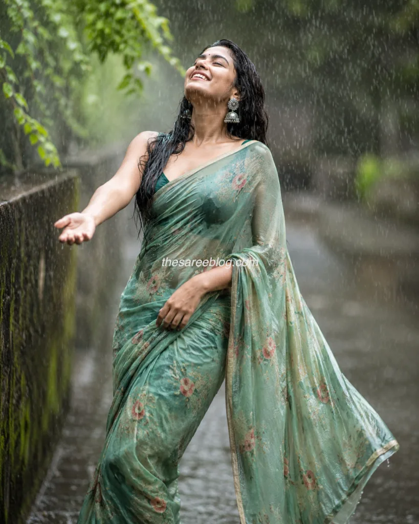 Woman wearing a teal georgette saree with a printed blouse, walking confidently on a rain-soaked street during the monsoon with a chic crossbody bag.